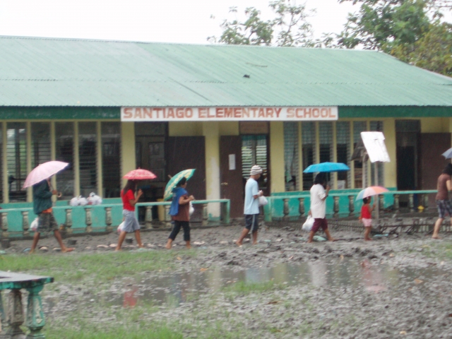 Braving the rain and mud to get their small share of OMASC blessing. At the height of the flood, water rose almost halfway from floor to ceiling of that school building.